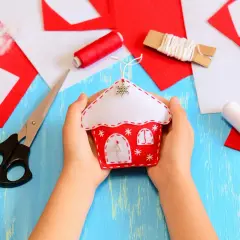 Dziecko trzyma w dłoniach filcowy domek, jeden z gotowych wzorów z filcu. Wokół nożyczki, nici i skrawki filcu.