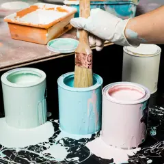 Puszki z farbą w pastelowych kolorach, pędzel w rękawiczce. Pamiętaj o odpowiedniej temperaturze przechowywania farb, by zachowały jakość.