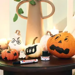 Inspiracja na to, jak pomalować dynie na Halloween: urocze duchy i straszne buźki na małych i dużych dyniach, obok pisak i tusz.