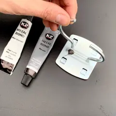 Dłoń trzyma metalowy element, obok tubki kleju K2 Metal Bond. Czy kropelka sklei metal? Zobaczymy!