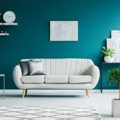 Elegancki salon z kanapą i roślinami na tle głębokiego turkus koloru ścian.