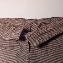 Brązowe spodnie w paski, z widocznym zapięciem na guzik i zamek.