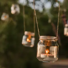 Uroczy lampion ze słoika z płonącą świecą, wiszący wśród zieleni.