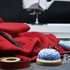 Czerwona tkanina, maszyna do szycia, szpilki, miarka i nożyczki. Idealne do tworzenia patchwork wzory.