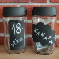 Dwie skarbonki ze słoików. Jedna z napisem "18. stka", druga z napisem "Kanapa" i widocznymi monetami oraz banknotem.