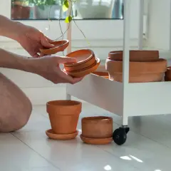 Mężczyzna układa gliniane osłonki na doniczkę 10 cm na białym wózku.