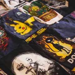 Stos koszulek z nadrukami: Iron Man, Pikachu, Jack Skellington, klawiatura. Zastanawiasz się, jak przykleić odklejający się nadruk na koszulce?