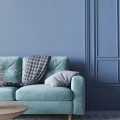 Miętowa kanapa z kocem i poduszką na tle ściany w odcieniu cyan blue.