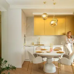 Elegancka kuchnia z błyszczącymi, stare złoto kolor szafkami. Okrągły stół z krzesłami czeka na gości.