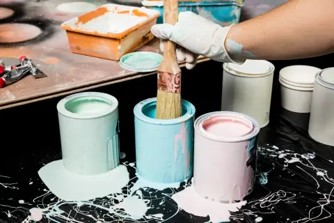 Puszki z farbą w pastelowych kolorach, pędzel w rękawiczce. Pamiętaj o odpowiedniej temperaturze przechowywania farb, by zachowały jakość.