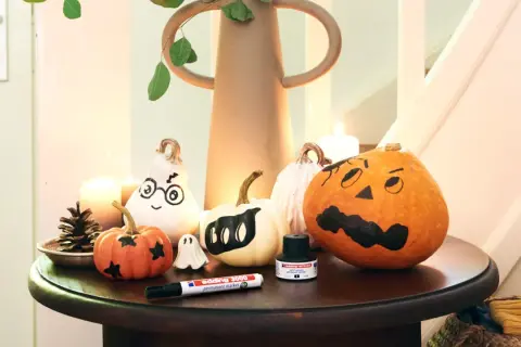 Inspiracja na to, jak pomalować dynie na Halloween: urocze duchy i straszne buźki na małych i dużych dyniach, obok pisak i tusz.