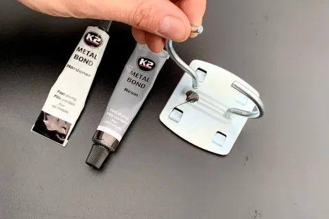 Dłoń trzyma metalowy element, obok tubki kleju K2 Metal Bond. Czy kropelka sklei metal? Zobaczymy!