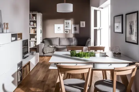 Nowoczesny salon z szarą kanapą i drewnianymi meblami. Dominują kolory brąz i szary, tworząc przytulną atmosferę.
