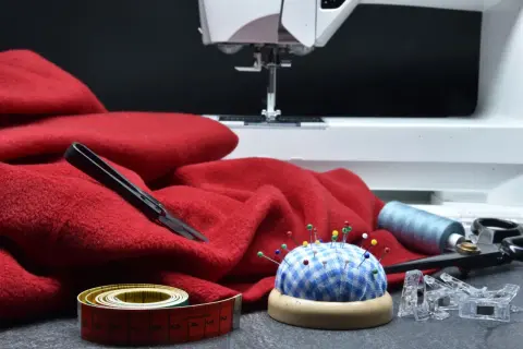 Czerwona tkanina, maszyna do szycia, szpilki, miarka i nożyczki. Idealne do tworzenia patchwork wzory.