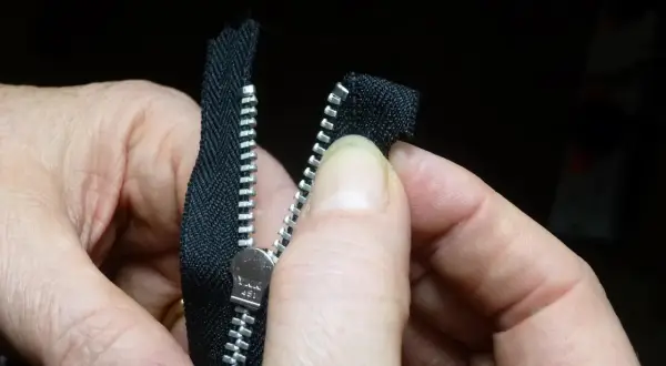 Dłonie pokazują, jak dobrać suwak do zamka. Metalowy suwak YKK 451 jest dopasowywany do czarnego zamka.