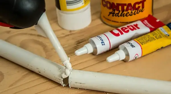 Klej w tubce jest aplikowany na pękniętą białą rurkę. Obok leżą tubki z klejem i puszka "Contact Adhesive". Czy kropelka sklei plastik?