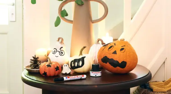 Inspiracja na to, jak pomalować dynie na Halloween: urocze duchy i straszne buźki na małych i dużych dyniach, obok pisak i tusz.