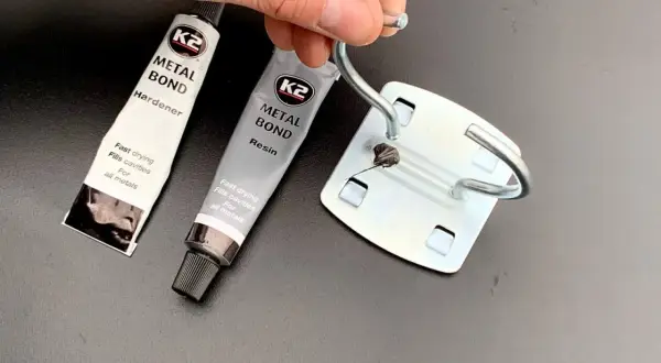 Dłoń trzyma metalowy element, obok tubki kleju K2 Metal Bond. Czy kropelka sklei metal? Zobaczymy!