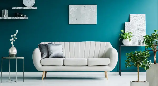 Elegancki salon z kanapą i roślinami na tle głębokiego turkus koloru ścian.
