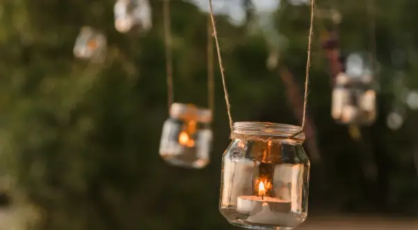 Uroczy lampion ze słoika z płonącą świecą, wiszący wśród zieleni.