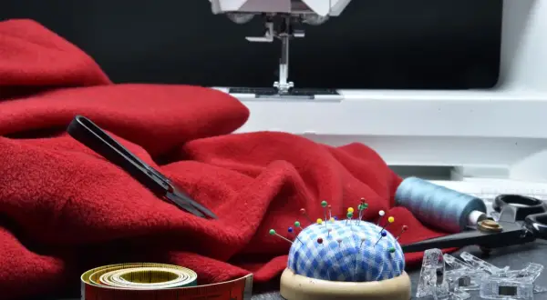 Czerwona tkanina, maszyna do szycia, szpilki, miarka i nożyczki. Idealne do tworzenia patchwork wzory.