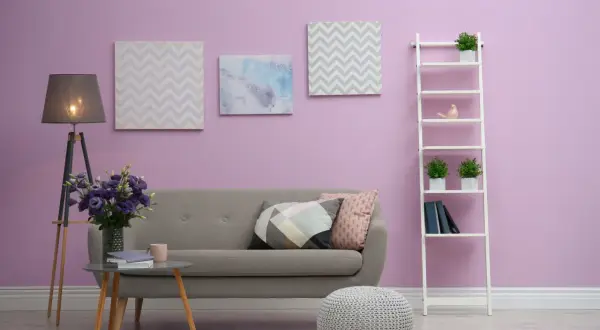 Przytulny salon z szarą kanapą, stolikiem kawowym, lampą i dekoracjami na półce. Ściana w odcieniu kolor lila róż.