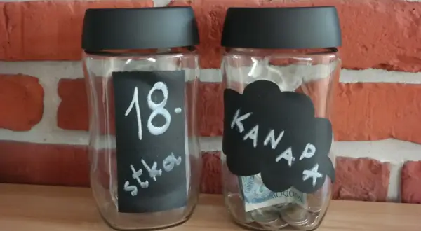 Dwie skarbonki ze słoików. Jedna z napisem "18. stka", druga z napisem "Kanapa" i widocznymi monetami oraz banknotem.