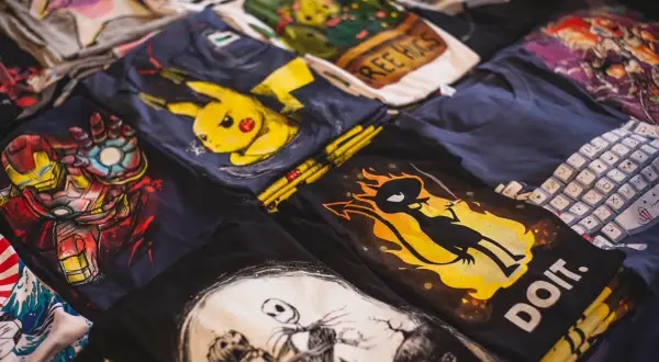 Stos koszulek z nadrukami: Iron Man, Pikachu, Jack Skellington, klawiatura. Zastanawiasz się, jak przykleić odklejający się nadruk na koszulce?