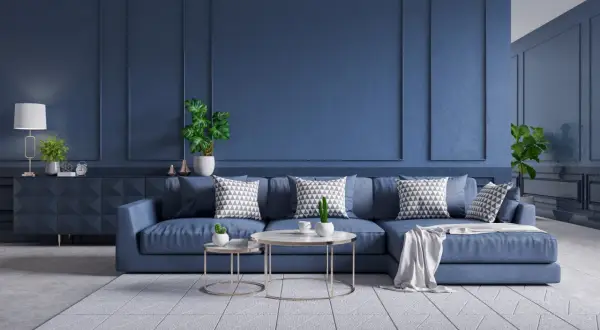 Nowoczesny salon z sofą w kolorze petrol blue, ozdobioną geometrycznymi poduszkami. Ściany w tym samym odcieniu tworzą spójną, elegancką całość.