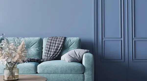 Miętowa kanapa z kocem i poduszką na tle ściany w odcieniu cyan blue.