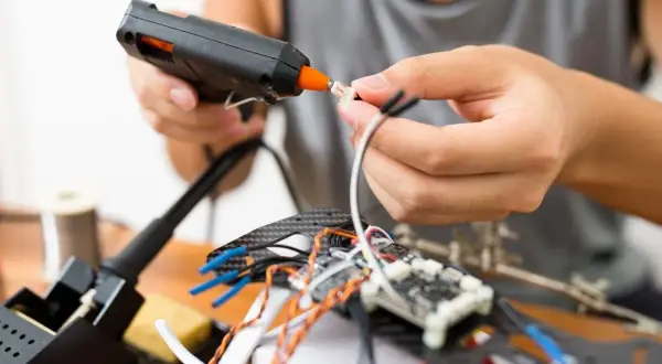 Ręce składają elektronikę, używając pistoletu na gorący klej. To szybki sposób, czym skleić metal i inne materiały przy majsterkowaniu.