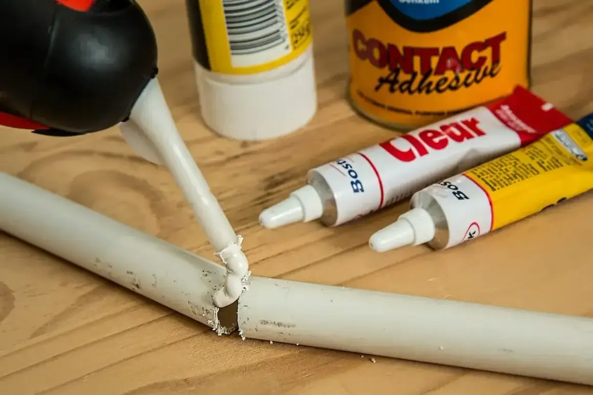 Klej w tubce jest aplikowany na pękniętą białą rurkę. Obok leżą tubki z klejem i puszka "Contact Adhesive". Czy kropelka sklei plastik?