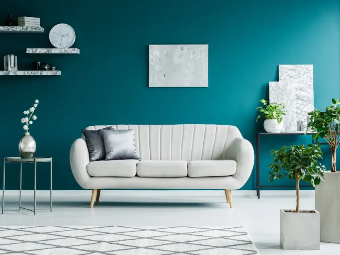 Elegancki salon z kanapą i roślinami na tle głębokiego turkus koloru ścian.