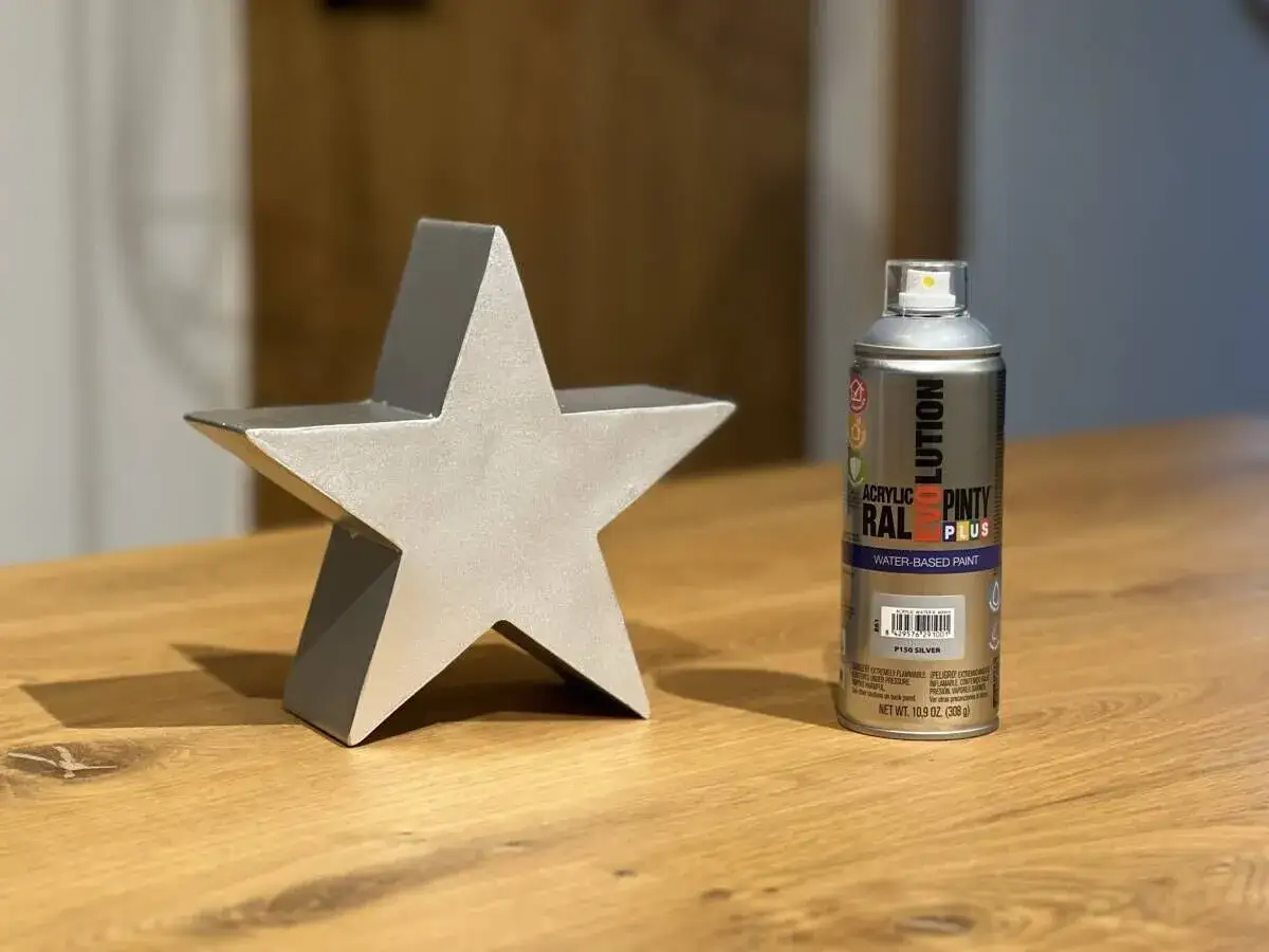 Srebrna gwiazda ozdobna obok puszki farby metalicznej w sprayu.