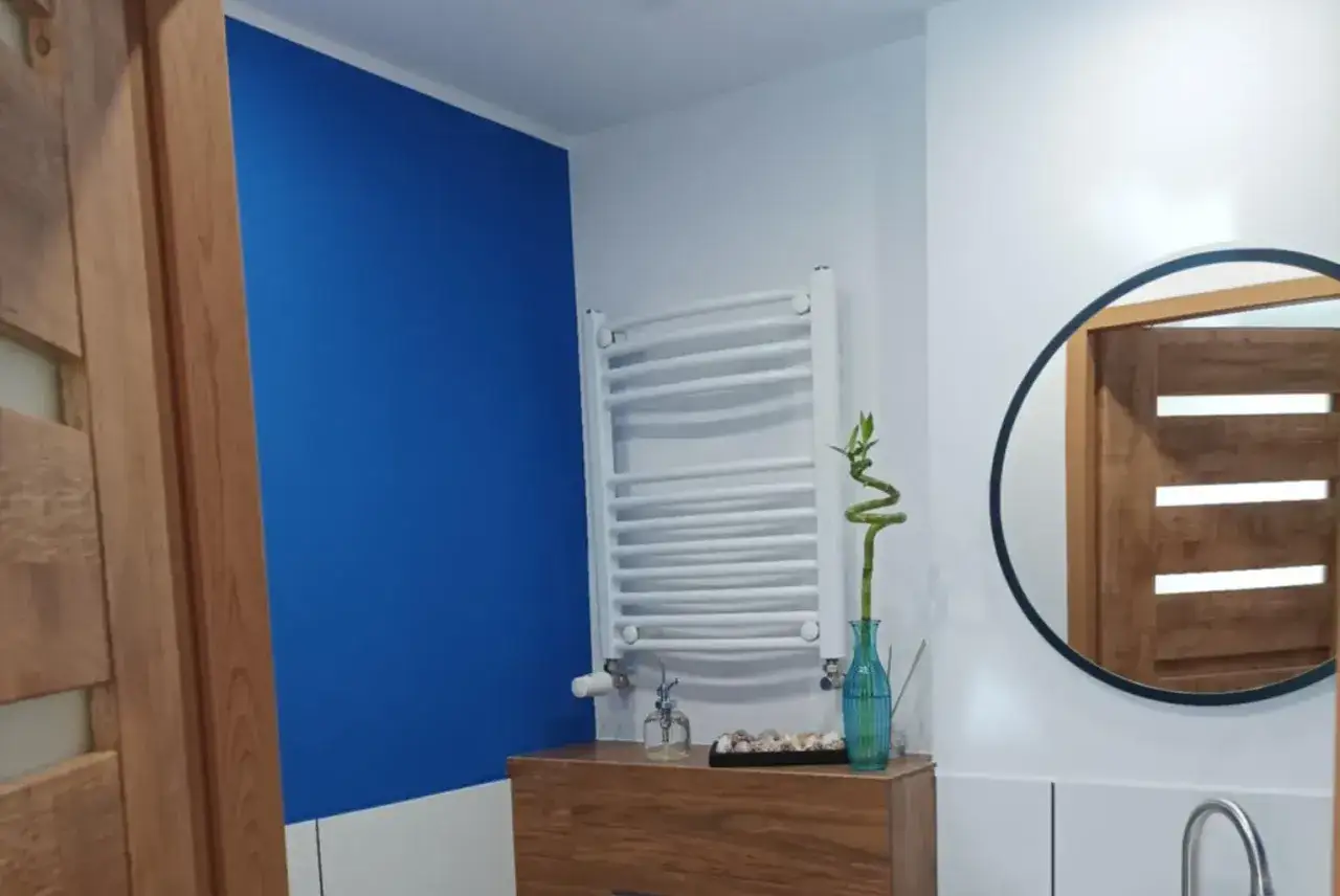 Łazienka z akcentem cobalt blue na ścianie, drewnianymi drzwiami i okrągłym lustrem.