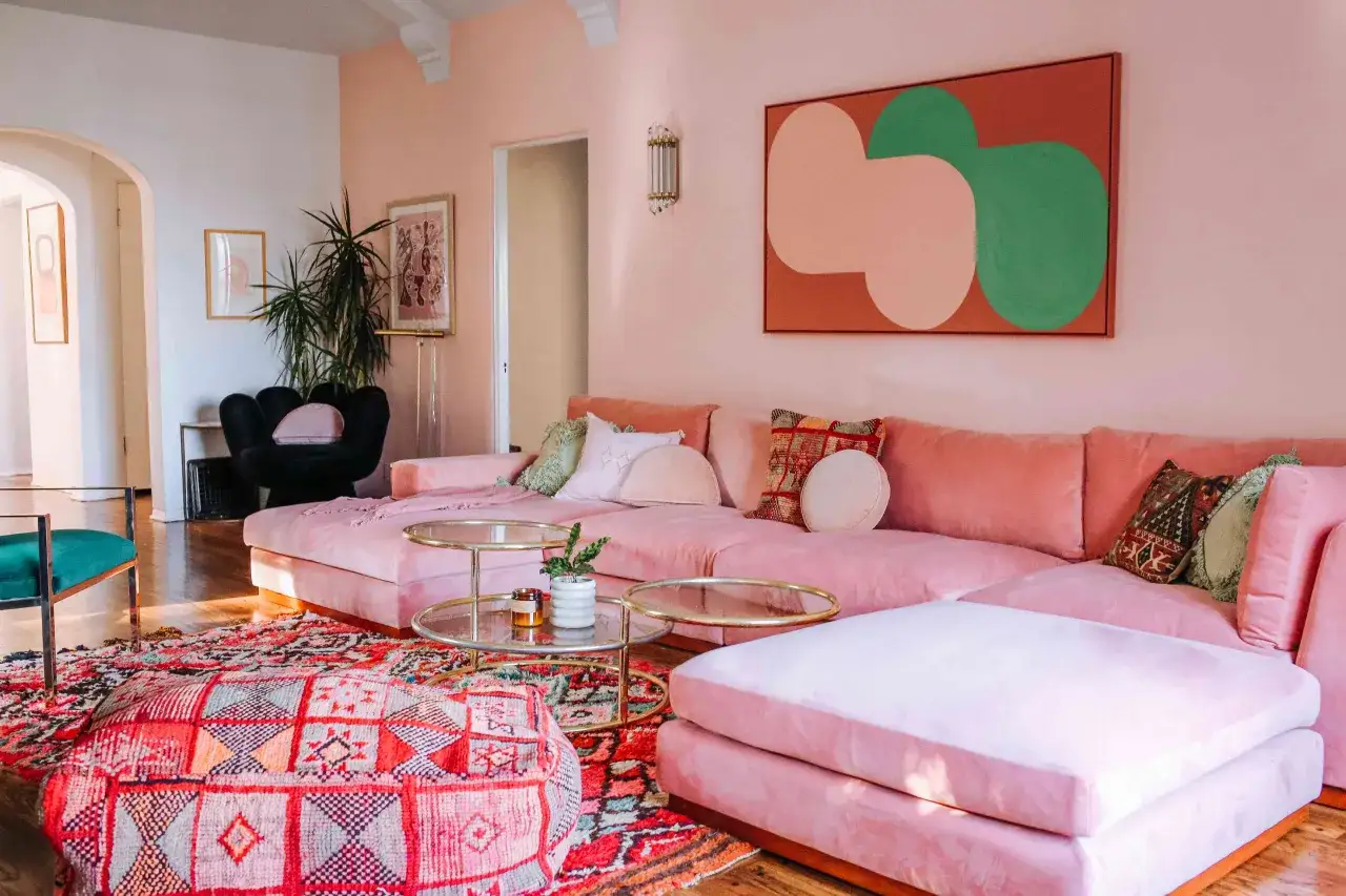 Przytulny salon w odcieniach millenial pink, z dużą różową kanapą, kolorowym dywanem i abstrakcyjnym obrazem.