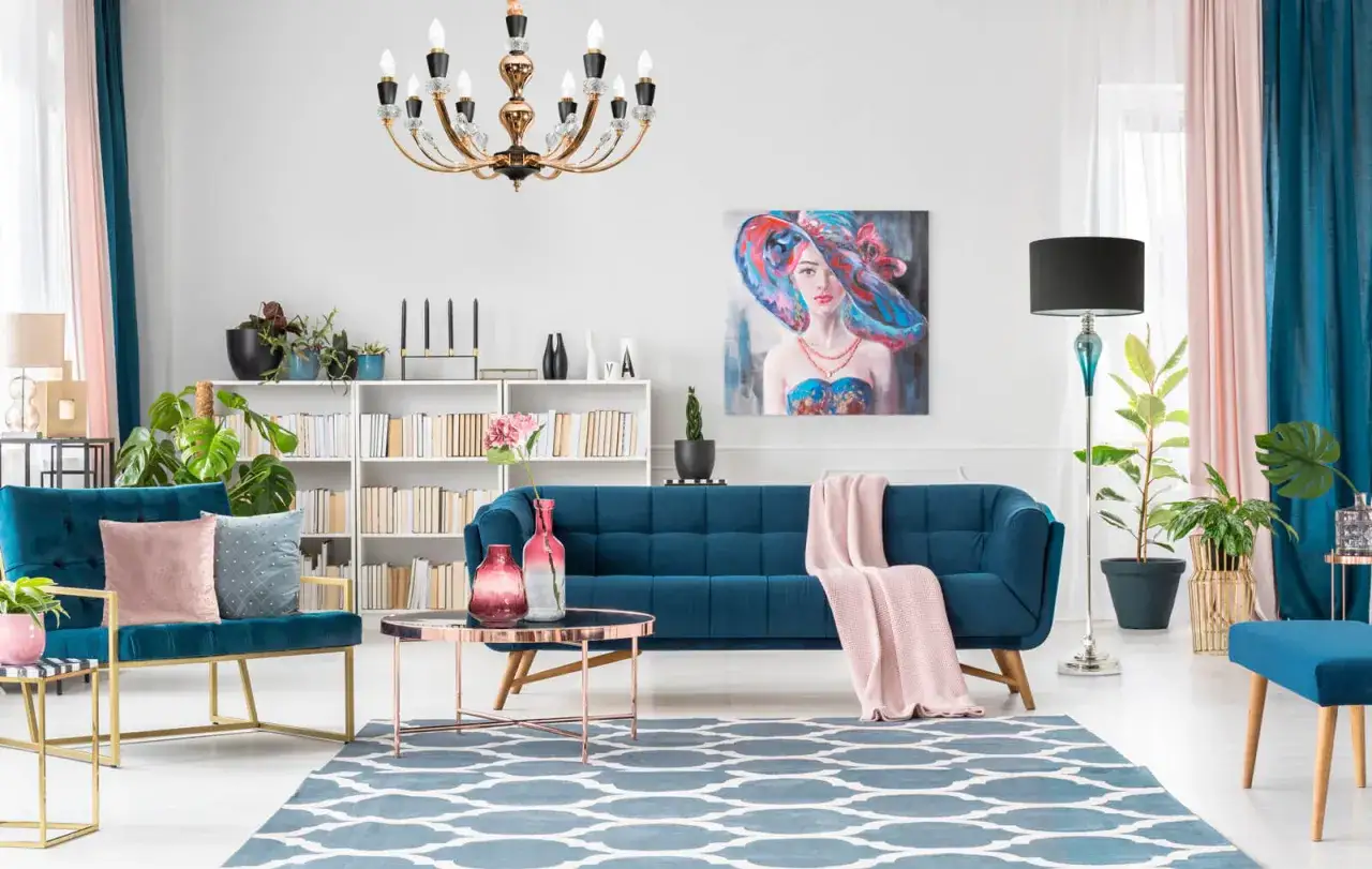 Elegancki salon z granatową kanapą, dywanem w geometryczne wzory w odcieniach kolor błękit, obrazem kobiety w kapeluszu i złotymi dodatkami.