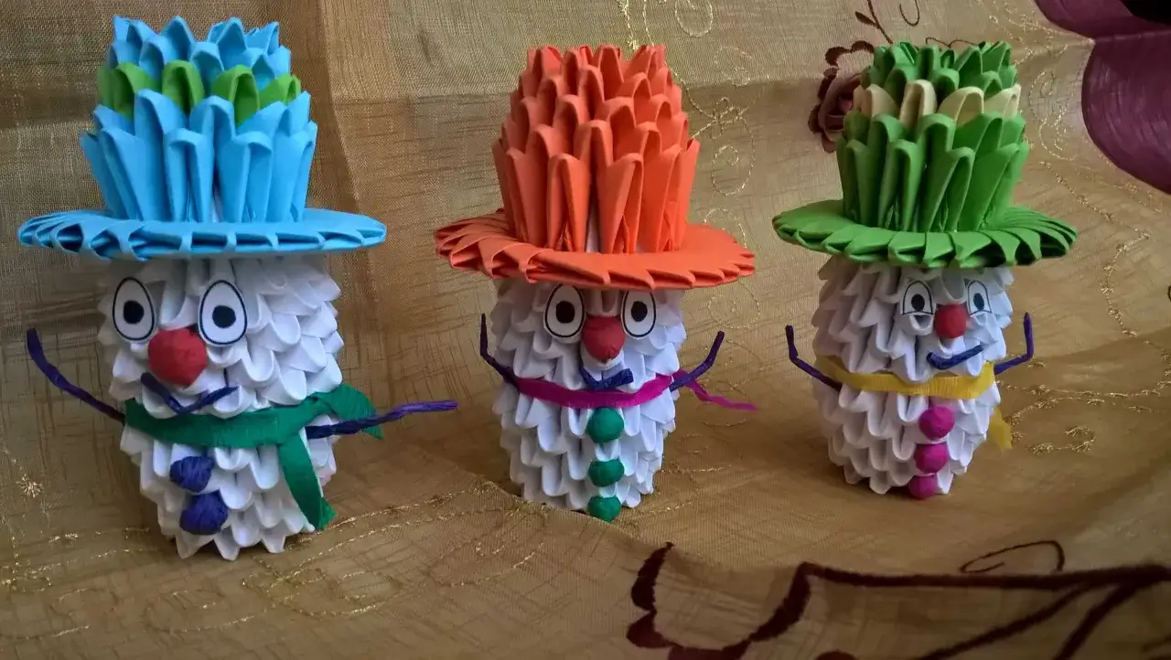 Trzy urocze bałwanki z origami, każdy w kolorowym kapeluszu, tworzą radosny zimowy widok.