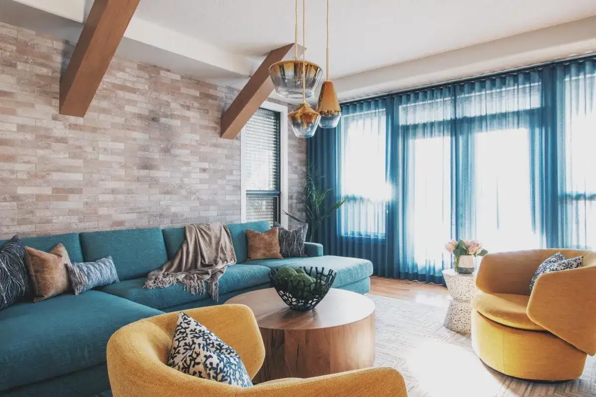Nowoczesny salon z kanapą w odcieniu cyan blue, żółtymi fotelami i ceglaną ścianą.