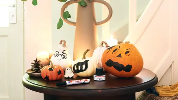 Inspiracja na to, jak pomalować dynie na Halloween: urocze duchy i straszne buźki na małych i dużych dyniach, obok pisak i tusz.