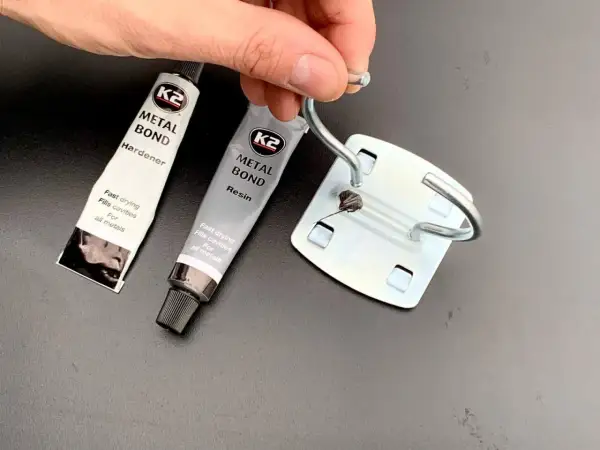 Dłoń trzyma metalowy element, obok tubki kleju K2 Metal Bond. Czy kropelka sklei metal? Zobaczymy!