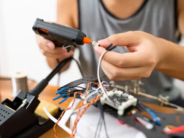 Ręce składają elektronikę, używając pistoletu na gorący klej. To szybki sposób, czym skleić metal i inne materiały przy majsterkowaniu.